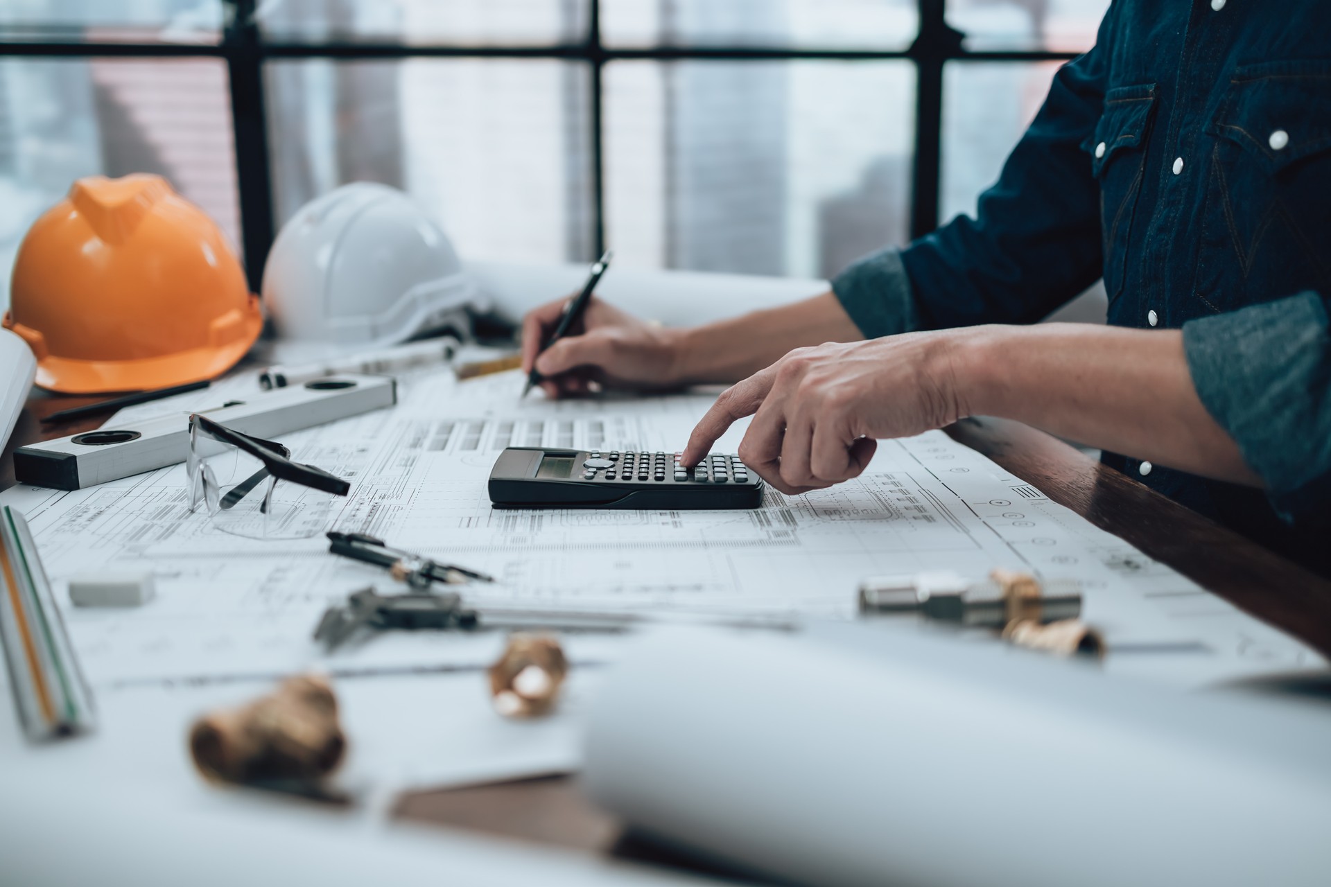 Engineering working with drawings inspection and press calculator on the office desk and triangle ruler, safety glasses, compass, verniear caliper on Blueprint. Engineer, Architect, Industy and factory concept.